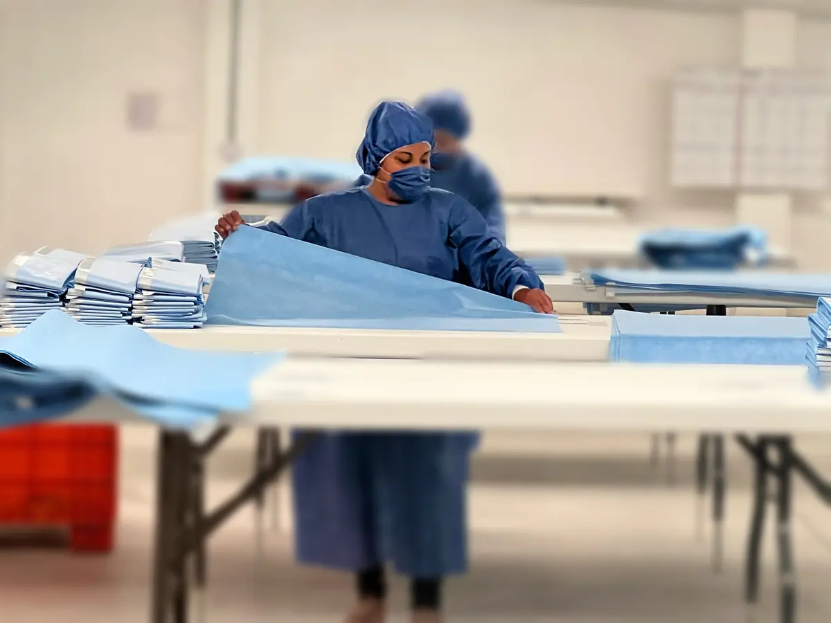 Una operaria dobla campos quirúrgicos azules sobre las mesas de trabajo